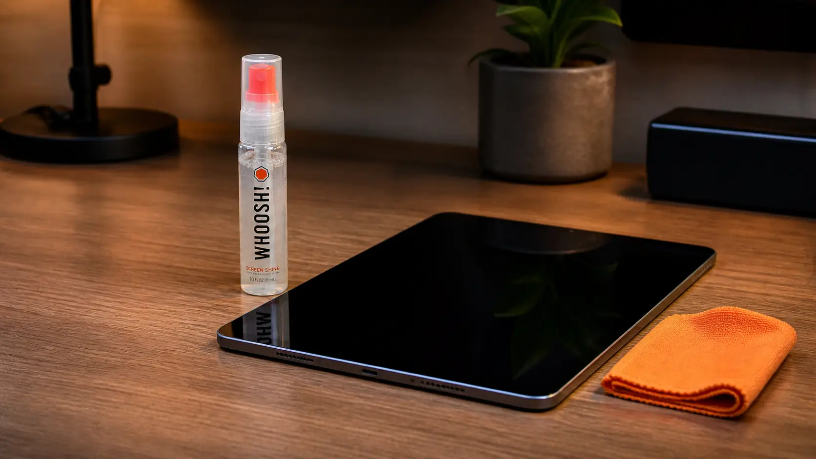 WHOOSH! Screen Shine spray and an orange microfiber cloth cleaning a tablet screen.